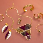 7 gold women's jewelry accessories neatly aligned around each other on top of a pink background casting light shadows.