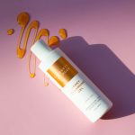 A bottle of honey cleansing gel on a pink background with honey drizzle