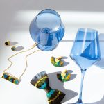 Men's bowtie and women's jewelry accessories next to blue wine glasses.