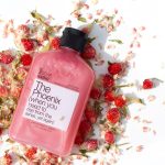 Pink body wash laying down on a bed of pink and red rose petals with a white background.