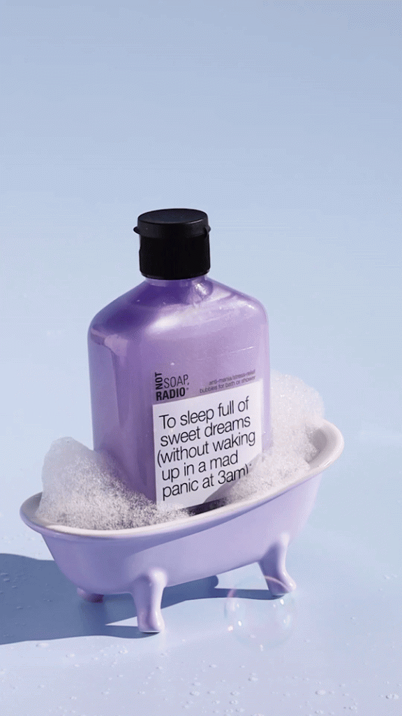 A purple soap in a mini bathtub with bubbles floating by.